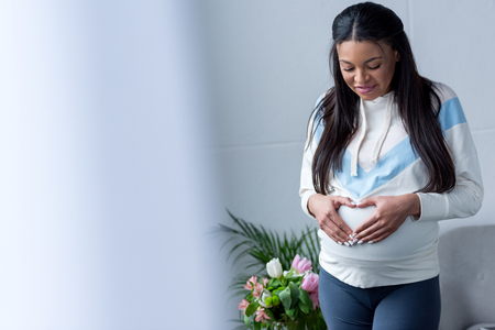 african american pregnant woman making heart symbol with hands on her bellyの写真素材