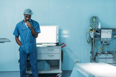 sad african american doctor standing in operating roomの写真素材