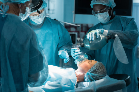 african american anesthetist holding oxygen mask above patient in surgery roomの写真素材