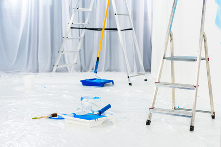 ladders and paint roller brushes in blue paint in roomの写真素材