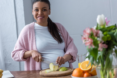 african american pregnant woman cutting apple at kitchenの写真素材