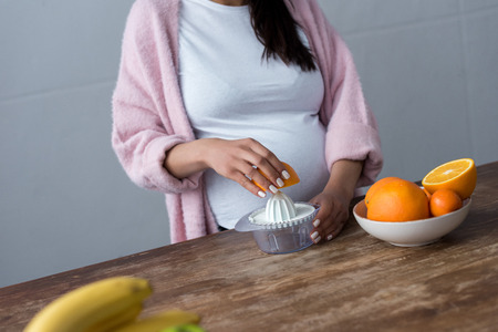 partial view of pregnant woman making orange juice with squeezerの写真素材