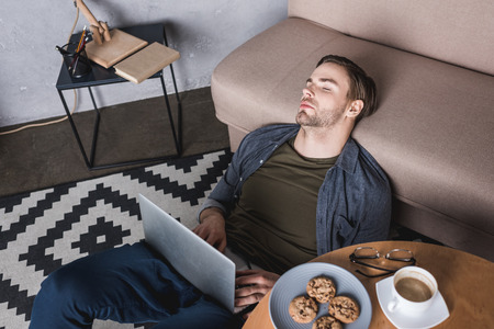 young overworked man sleeping on floor with laptop