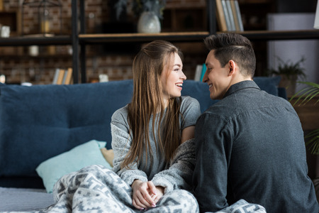 happy couple sitting on bed in morning and looking at each otherの写真素材