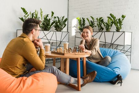 young happy friends playing chess while sitting on beanbagsの写真素材