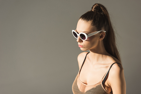 fashionable brunette girl with ponytail hairstyle in sunglasses, isolated on greyの写真素材