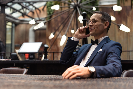 handsome adult man in suit talking by phone at restaurantの写真素材