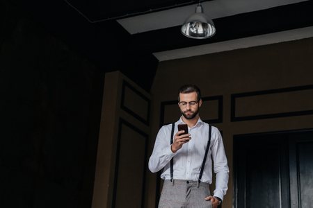 elegant bearded man in suspenders using smartphoneの写真素材