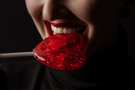 cropped image of woman biting heart shaped lollipop isolated on blackの写真素材