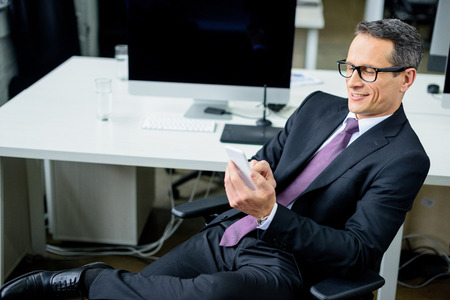 portrait of smiling businessman using smartphone at workplace
