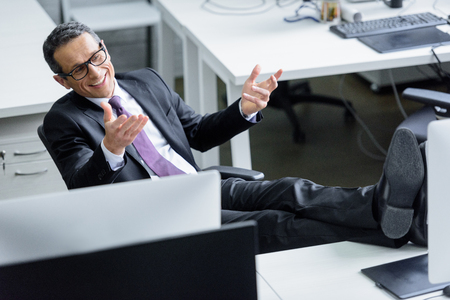 cheerful businessman in eyeglasses sitting at workplace in officeの写真素材