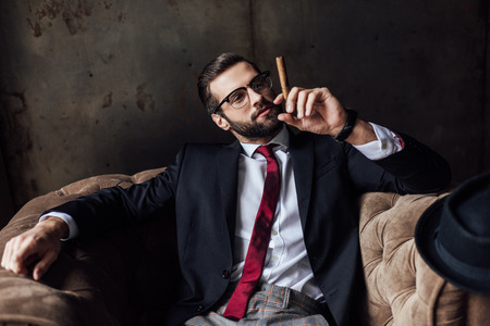 fashionable man sitting in armchair and holding cigarの写真素材