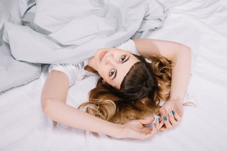 overhead view of girl lying under blanket with hands up and looking at cameraの写真素材