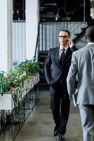 confident businessman talking on smartphone while walking in officeの写真素材
