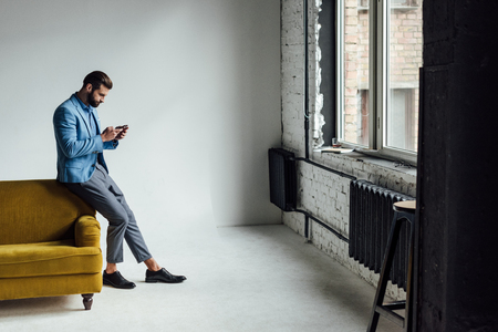fashionable man in blue suit using smartphone at yellow couchの写真素材