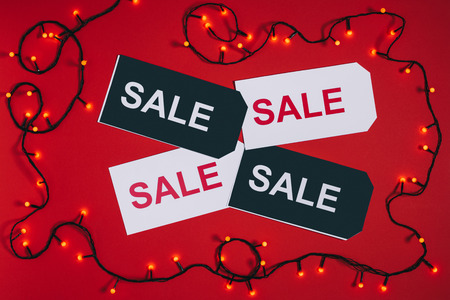 flat lay with price tags with sale lettering and christmas lights isolated on red