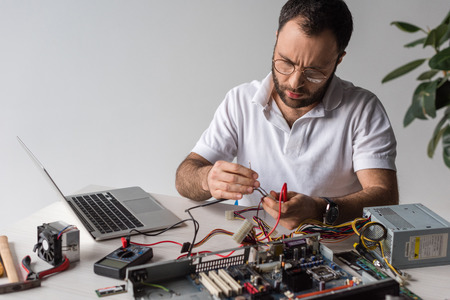 man using multimeter while fixing broken computer and looking down