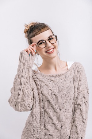 smiling girl standing and touching glasses isolated on whiteの写真素材