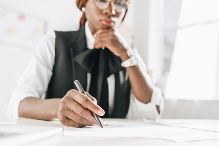 selective focus of african american female adult architect in glasses using pen and working on documents in officeの写真素材