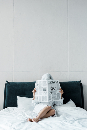 woman reading travel newspaper on bed in the morningの写真素材