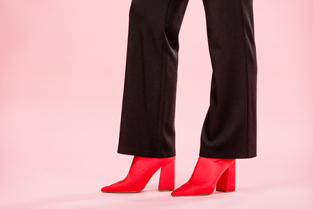 low section of young woman in stylish black pants and red shoes standing on pinkの写真素材