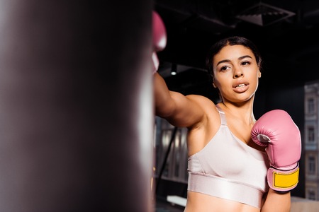 Attractive strong girl in pink boxing gloves practicing boxing in gymの写真素材