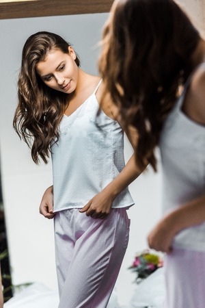beautiful slim girl in pajamas looking at her reflection in mirrorの写真素材