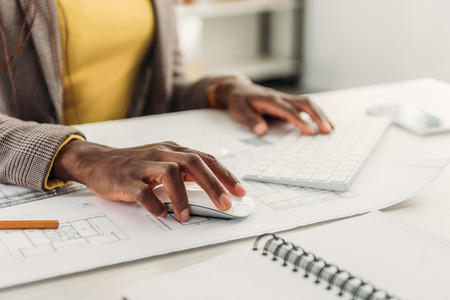 cropped view of african american female architect using compute desk with blueprintsの写真素材