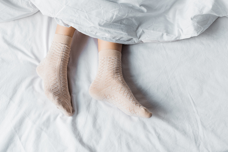 top partial view of girl in socks lying under white blanket in bedの写真素材