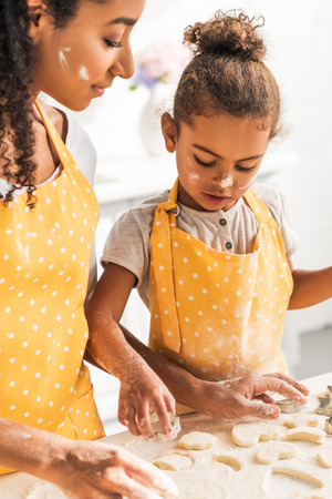 african american mother and daughter preparing cookies with dough molds in kitchenの写真素材