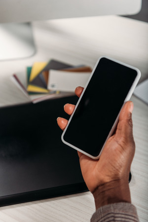 cropped view of african american female businesswoman holding coffee to go and smartphone with blank screenの写真素材