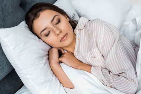 Beautiful young woman in pajamas sleeping on bedの写真素材