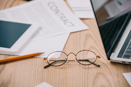 Close up view of eyeglasses, tablet, laptop and documents at workplace