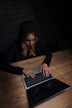 Woman in black hoodie using laptop, cyber security conceptの写真素材
