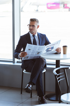 Adult handsome businessman in glasses reading newspaper in cafe at airportの写真素材