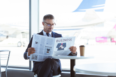 Adult businessman reading newspaper in cafe at airportの写真素材