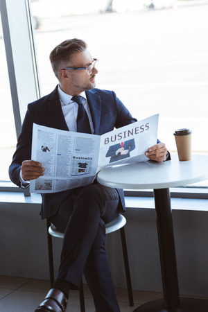 Adult businessman reading newspaper and looking at window at airportの写真素材