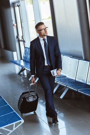 Adult businessman in glasses with baggage walking at airportの写真素材