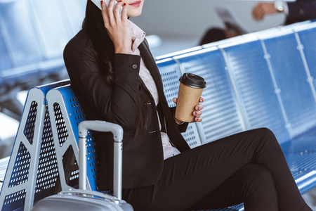 Close up of young businesswoman in glasses with baggage using smartphone at airportの写真素材