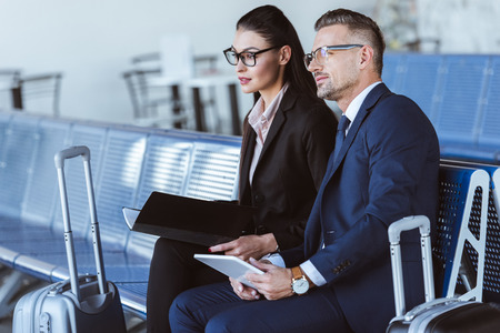 Adult businessman and businesswoman sitting at departure lounge in airportの写真素材