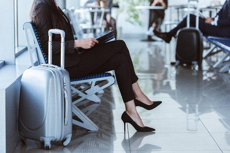 Businesswoman with black folder sitting at departure lounge in airportの写真素材