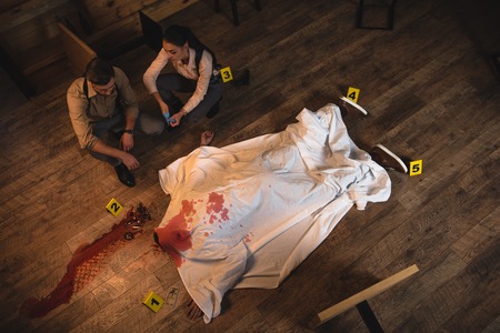 Female and male detectives investigating dead body covered with white sheet at crime sceneの写真素材