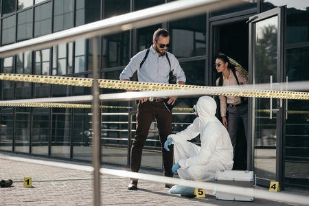 Detectives and criminologist  in protective suit and latex gloves communicating at crime sceneの写真素材