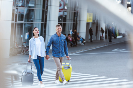 A couple of tourists crossing pedestrian, holding hands and pulling their luggageの写真素材