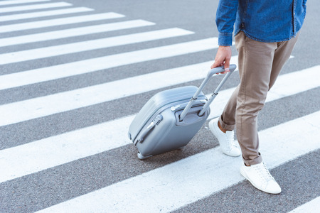 Cropped view of a tourist in white shoes with grey travel bagの写真素材
