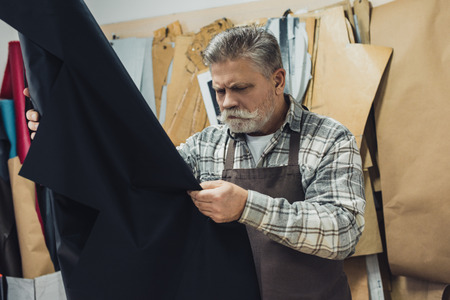 Concentrated handbag craftsman looking at leather in workshop