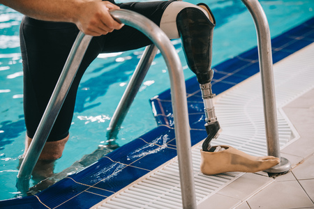 Cropped shot of swimmer with prosthetic leg getting out of swimming pool