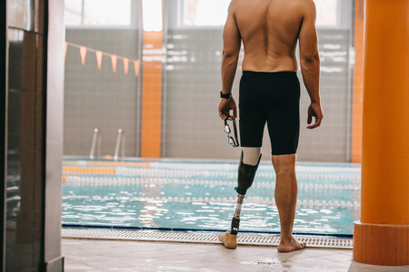 Cropped shot of sportsman with artificial leg standing in front of indoor swimming poolの写真素材
