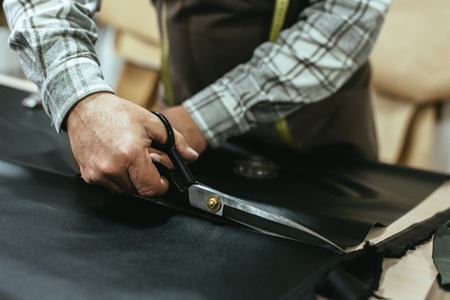 Partial view of male handbag craftsman cutting leather by scissors at studioの写真素材