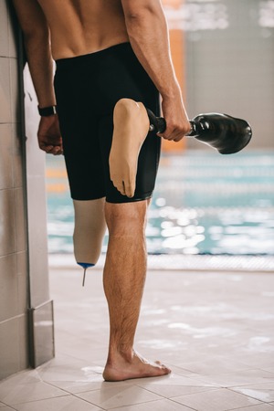 Cropped shot of sportsman standing at poolside of indoor swimming pool and holding his artificial legの写真素材